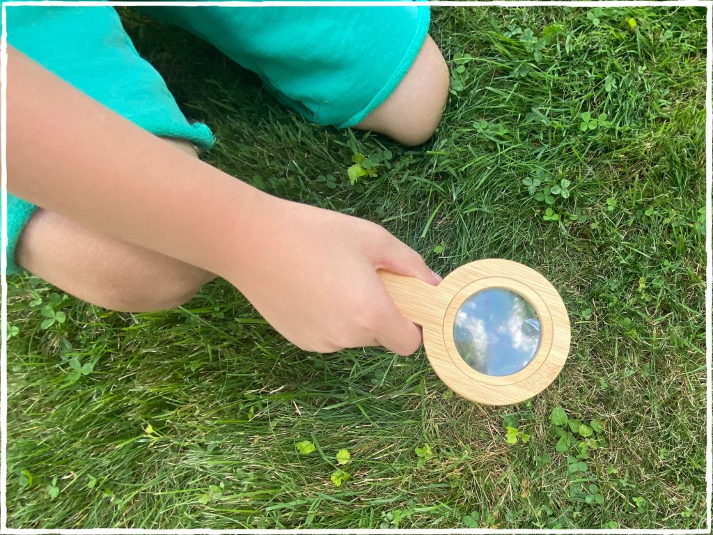My son kneeling down on a nature walk with a magnifying glass looking in the grass