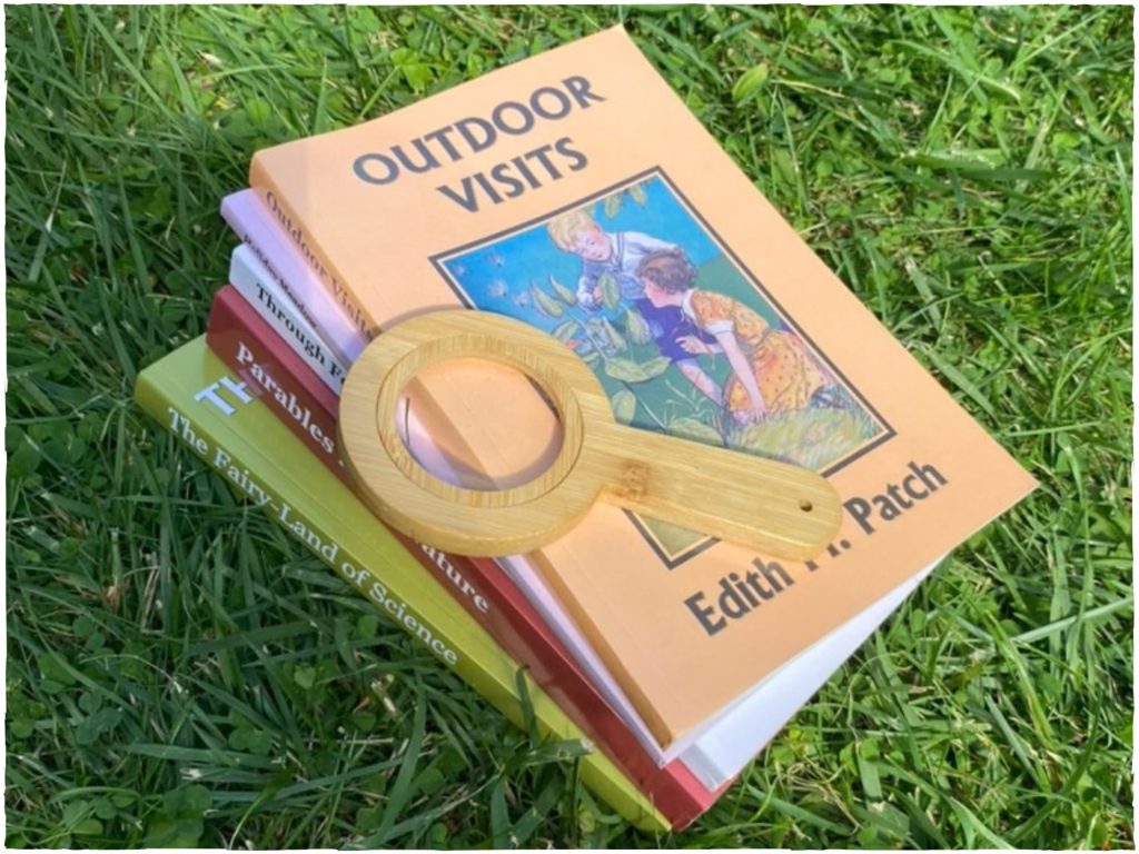 A series of beautiful nature books piled up with a magnifying glass on top